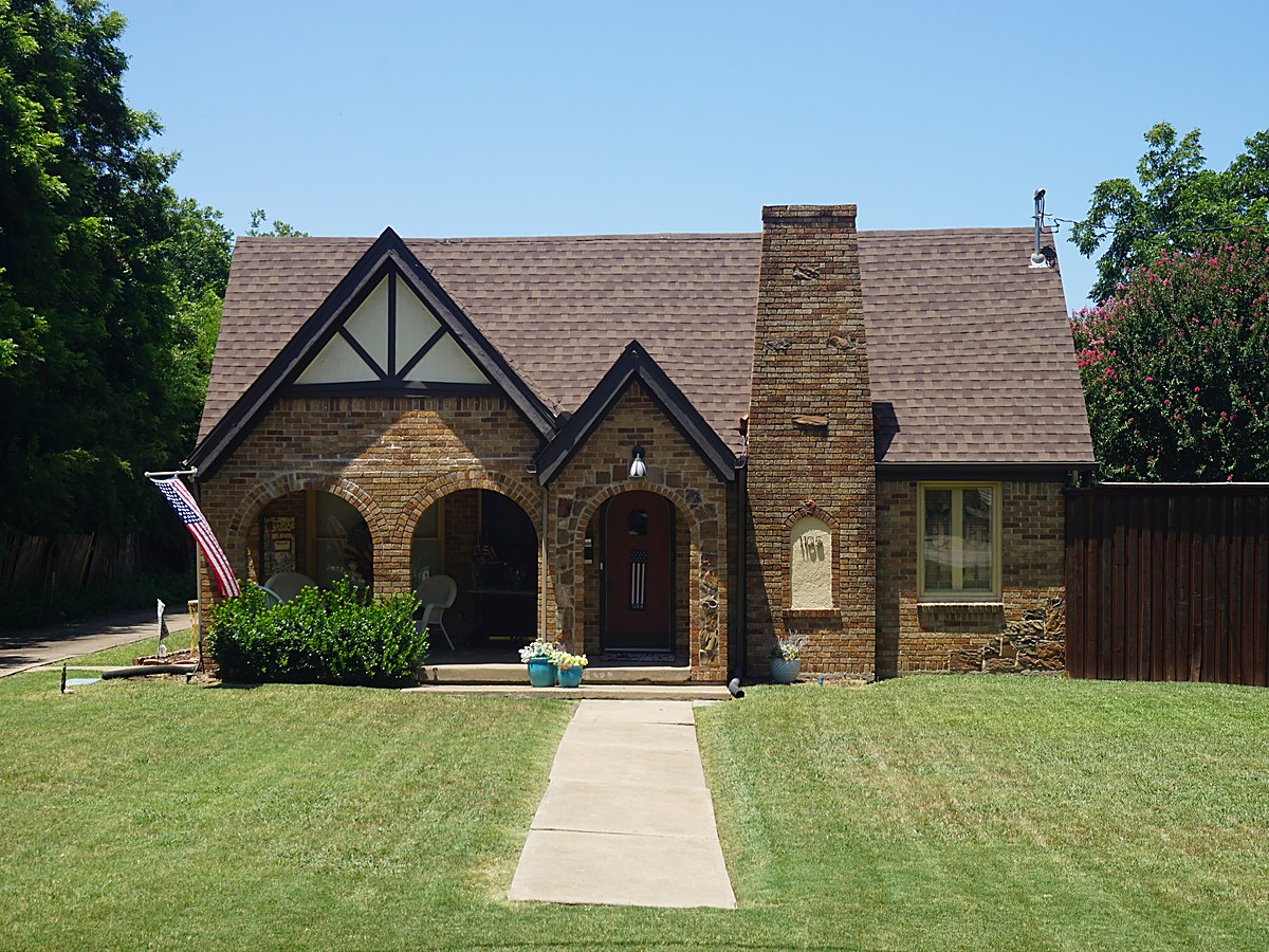 A Texas brick and stone house with a red tile roof and a mown lawn behind a low iron fence — representative imagery, not a specific Texas Pride job