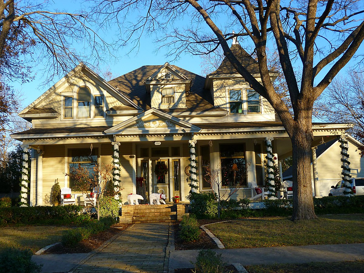 A large older timber-framed Texas house with a deep wraparound porch, seen through bare trees — representative imagery, not a specific Texas Pride job