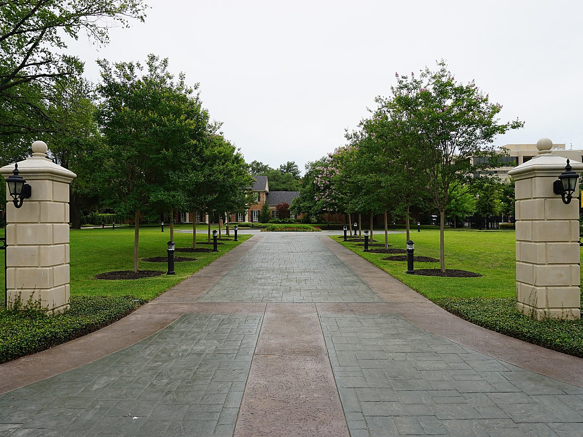 A landscaped entrance drive with stone gate posts leading into a wooded residential property — representative imagery, not a specific Texas Pride job